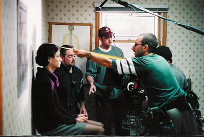 1st AC Marcello Duarte measures the distance from the focal plane to Nurit Monacelli.  Set Dresser Allen Doyle looks on in the background, and 1st AD Paul Epstein discusses with DP Tim Naylor.